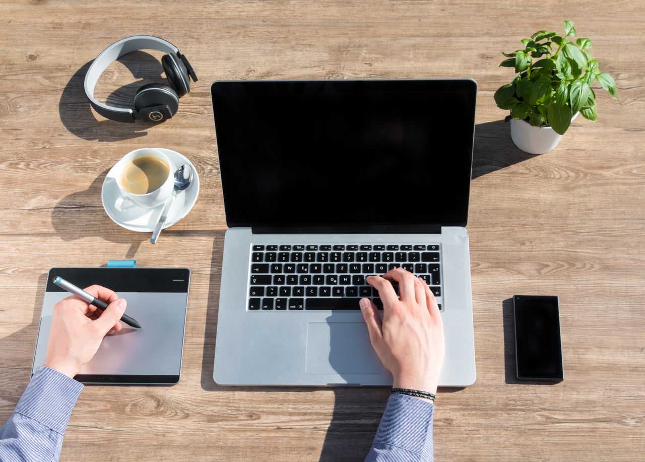 A stylish home office workspace featuring a laptop, drawing tablet, and coffee on a wooden desk.